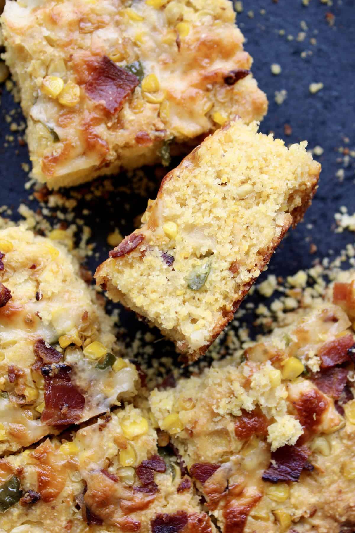 one slice of jalapeño bacon cornbread is tipped on its side in the cast iron skillet to reveal specks of jalapeño, corn kernels, and bacon