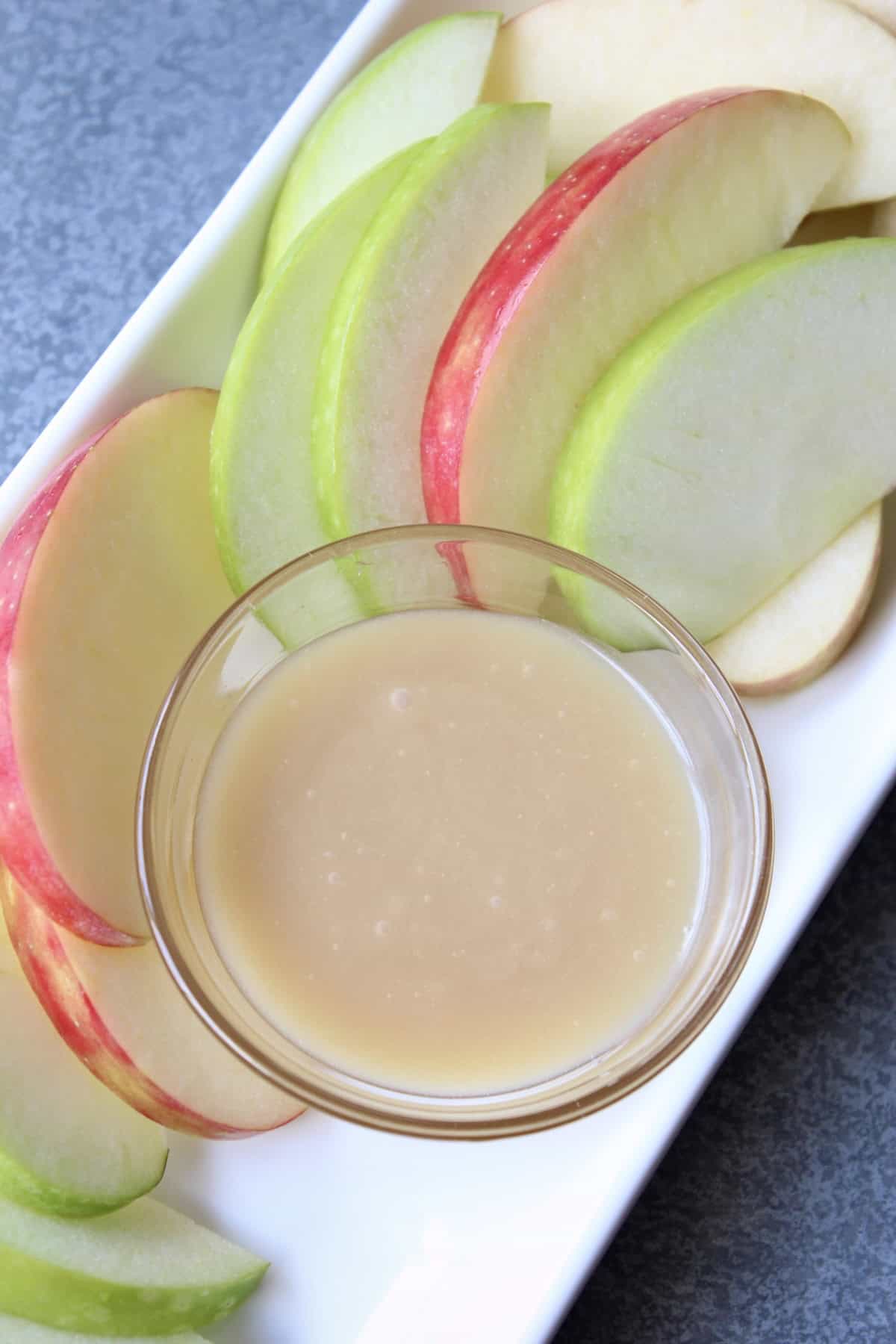 a small bowl of honey caramel sauce is placed in the center of a plate filled with apple slices