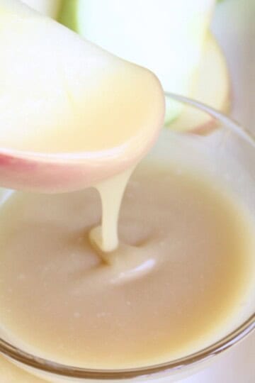 honey caramel sauce drizzles off the end of an apple slice as it is dipped into a bowl of the sauce