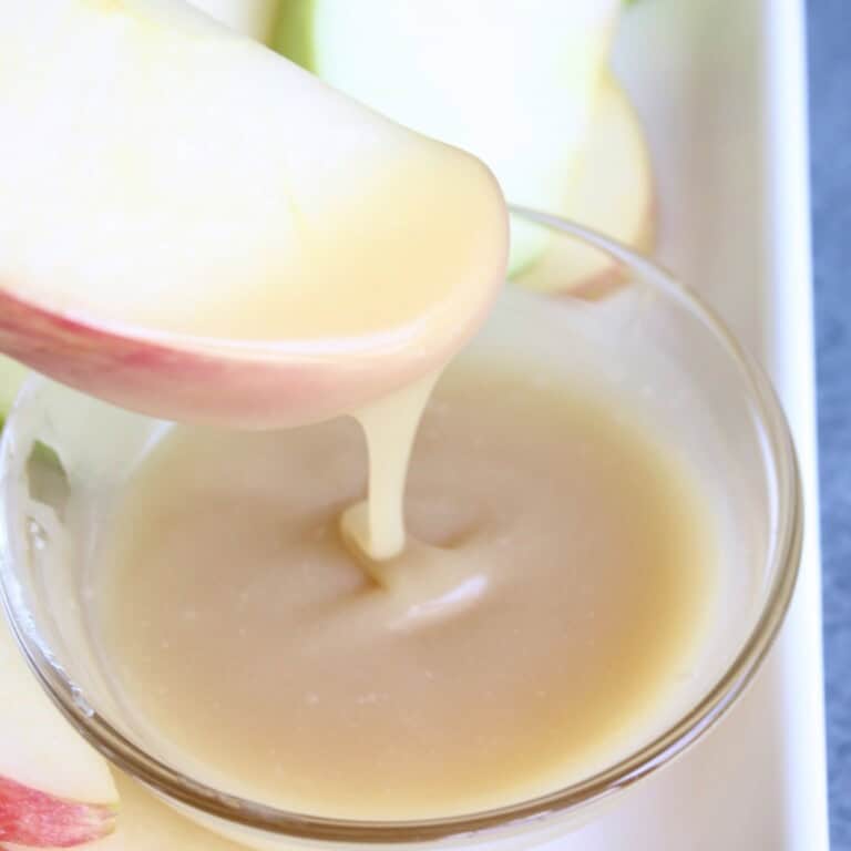 honey caramel sauce drizzles off the end of an apple slice as it is dipped into a bowl of the sauce