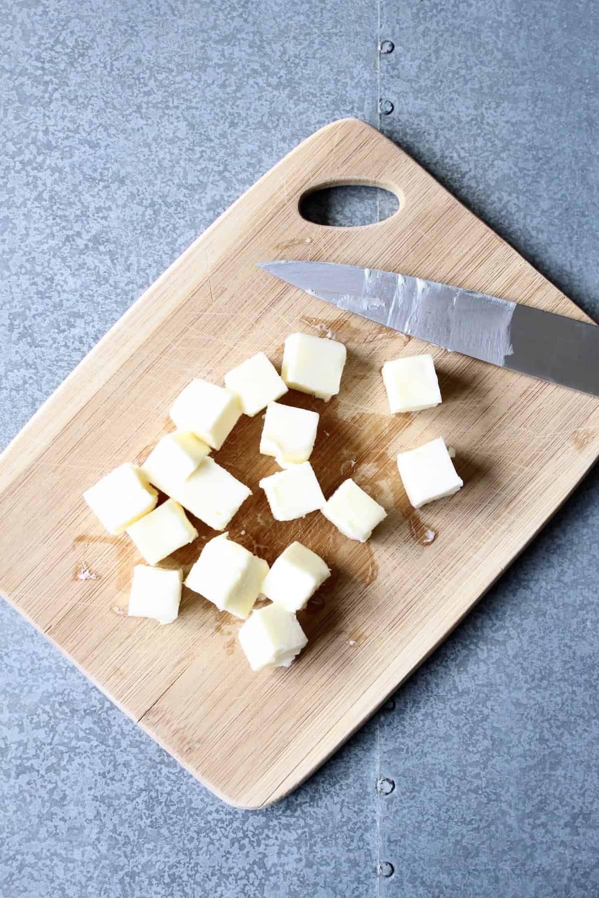 butter is sliced into smaller cubes on a wooden cutting board