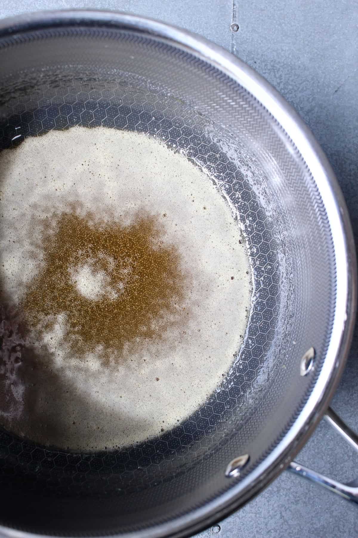a pot containing a mixture of honey and sugar turns deeply golden and slightly foamy as it cooks