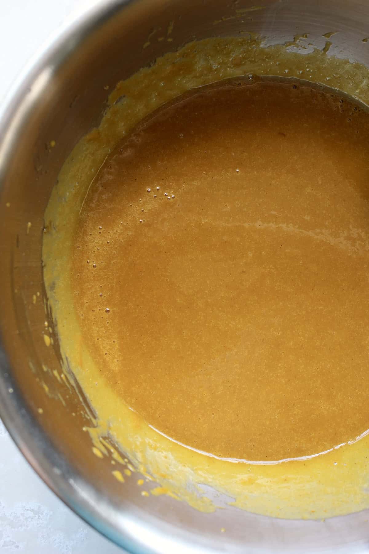 the wet ingredient mixture in a mixing bowl has a deep orange coloring and a smooth, glossy texture.