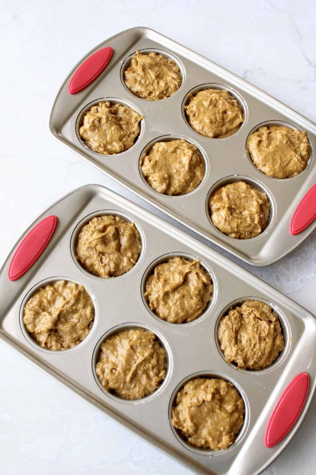 the pumpkin muffin batter is distributed between the cups of a 12 hole muffin pan