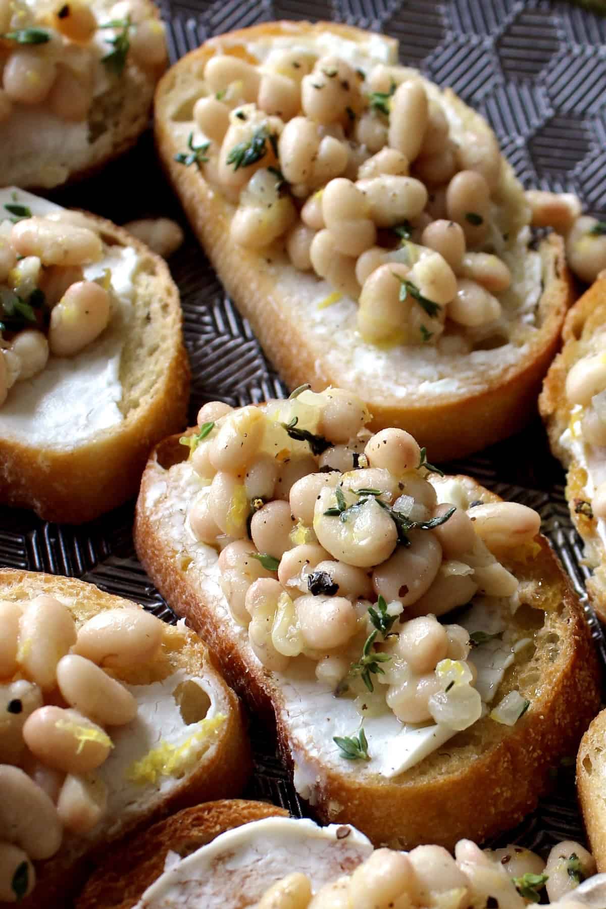 white bean bruschetta on a serving platter is garnished with thyme leaves and black pepper