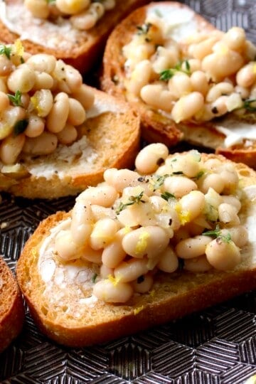 white bean bruschetta is arranged on a black geometric serving platter
