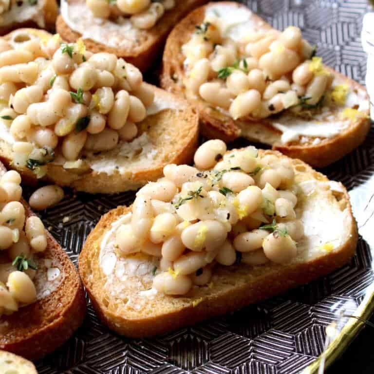 white bean bruschetta is arranged on a black geometric serving platter