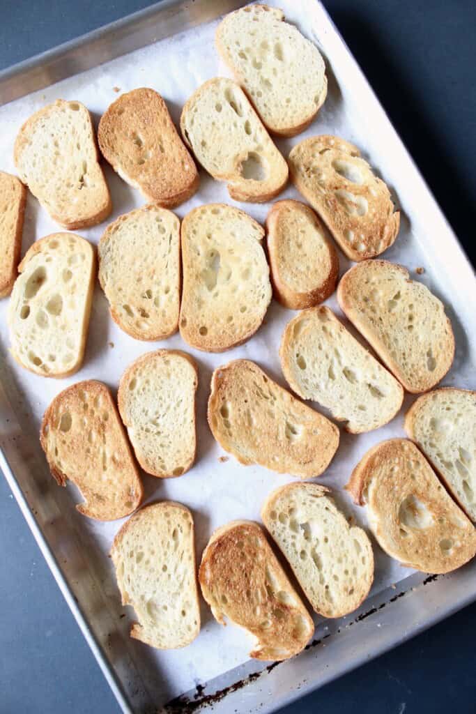 toasted slices of bread are arranged on a parchment paper lined baking sheet.